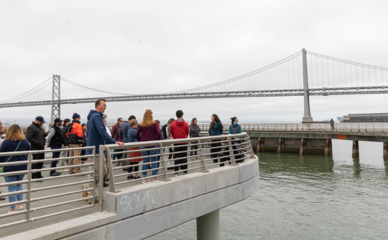 People standing on a pier overlooking the water and Bay Bridge