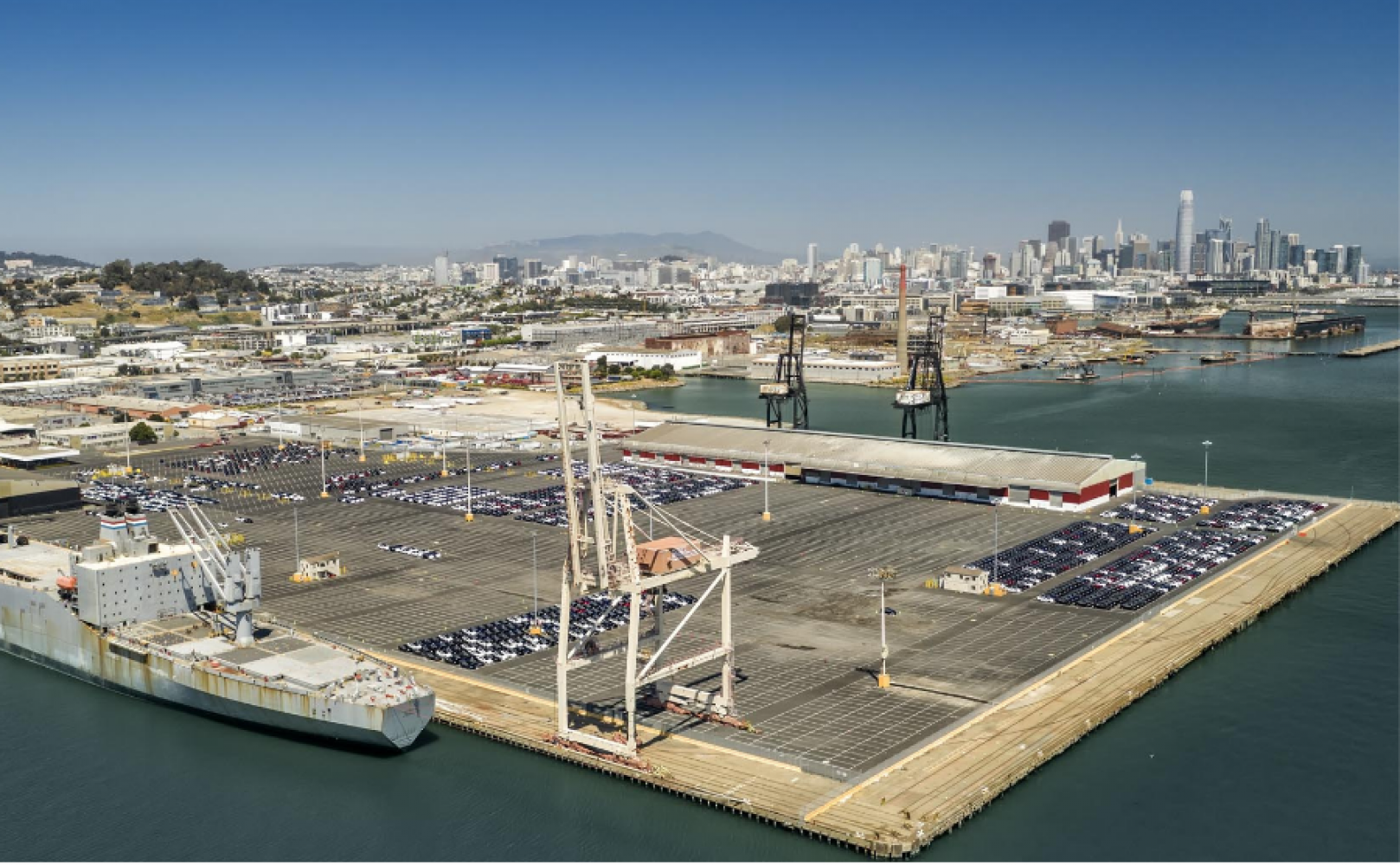 Cars parked in neat rows on a massive pier with cranes