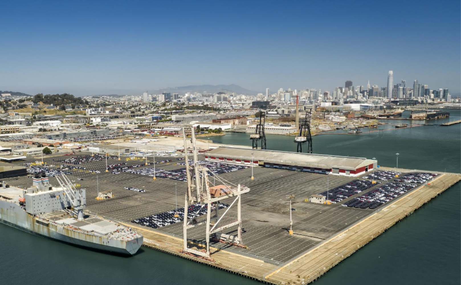 Cars parked in neat rows on a massive pier with cranes
