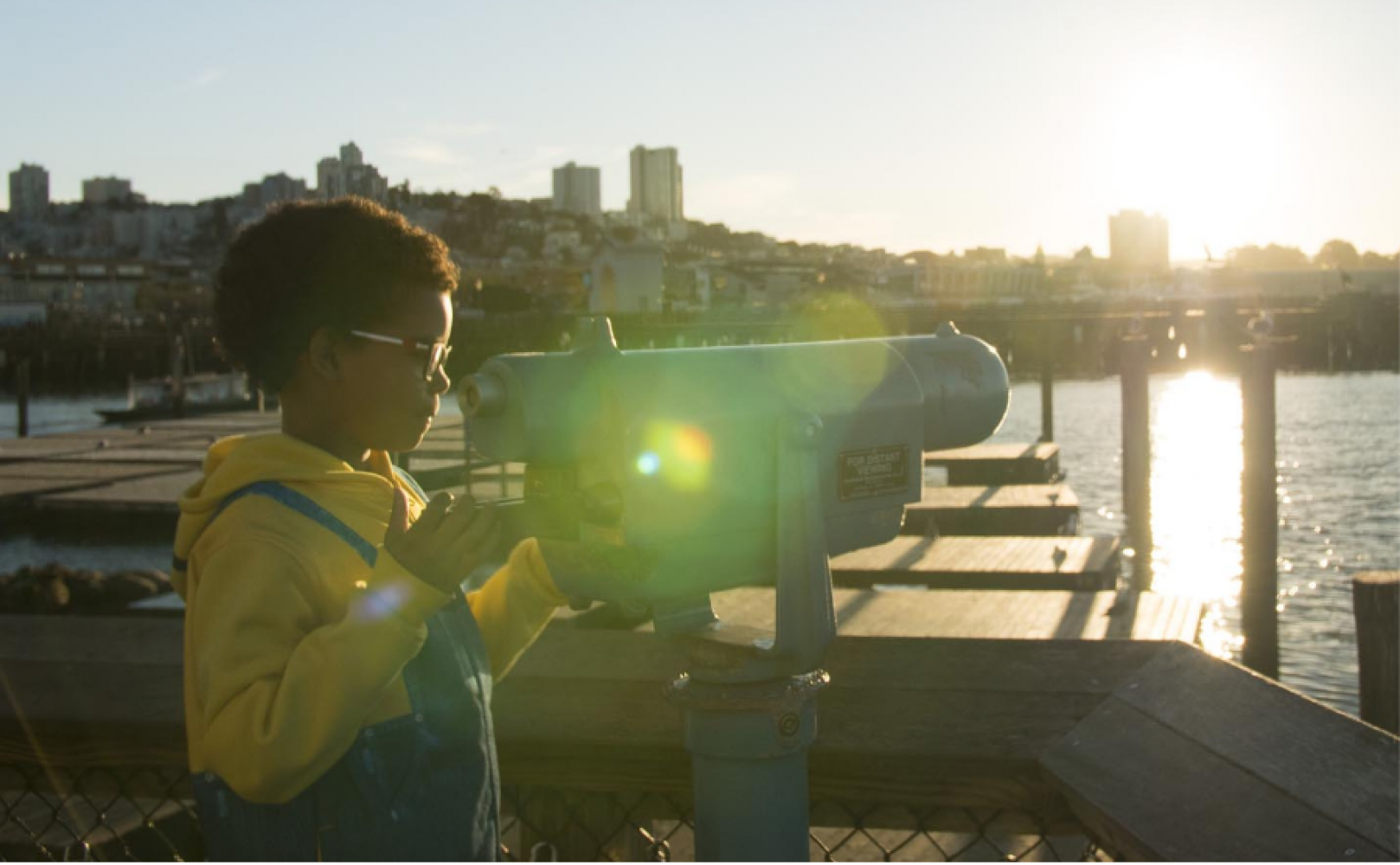Child looks through binoculars outside on the waterfront