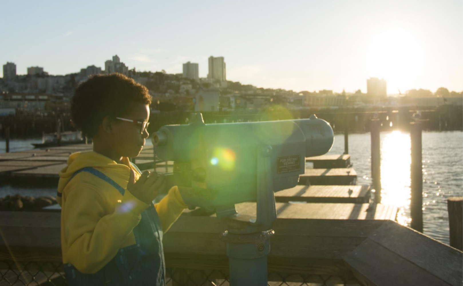 Child looks through binoculars outside on the waterfront