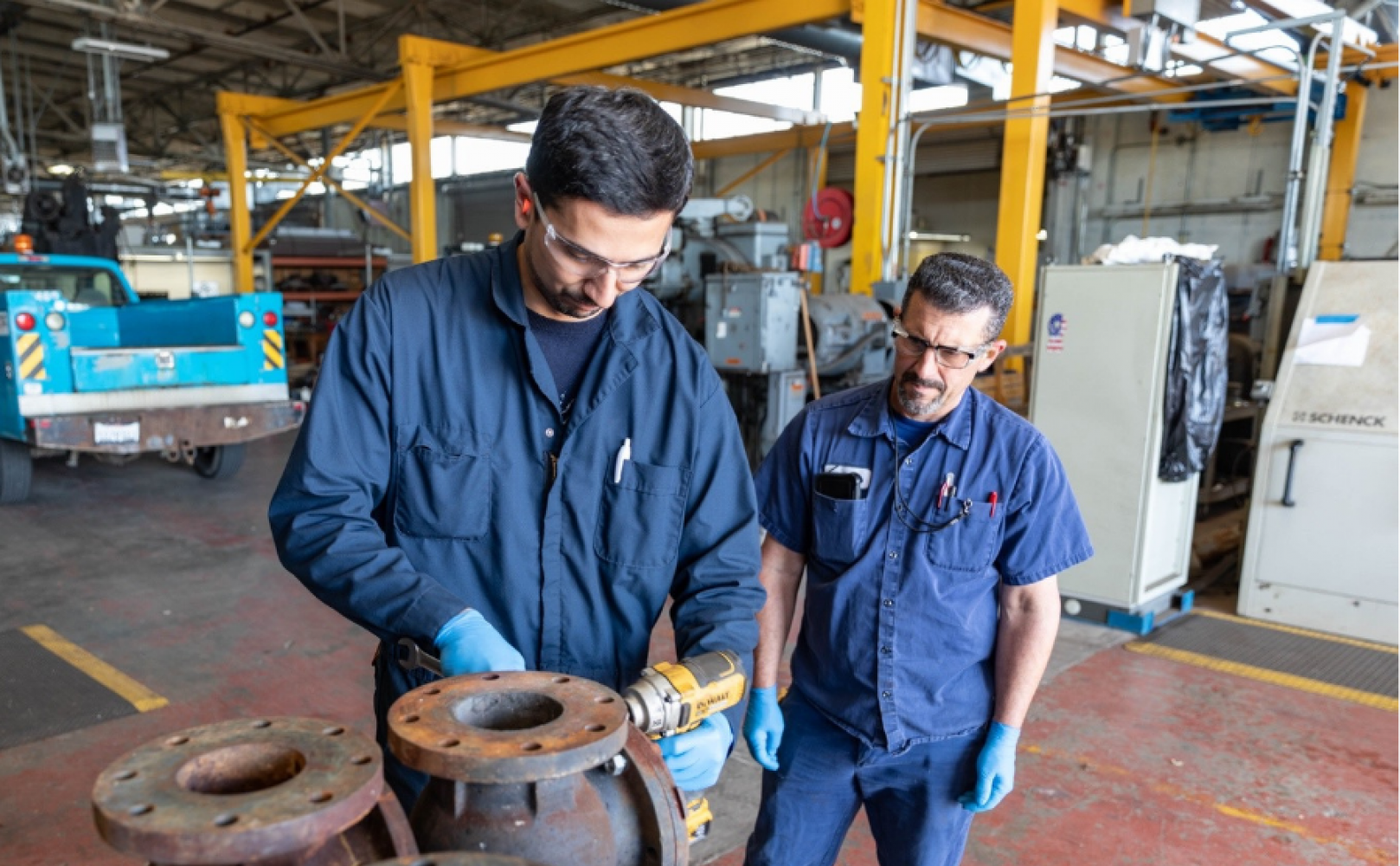 Man observes his trainee drill into a metal pipe.