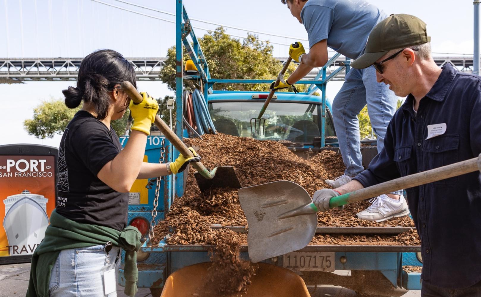 People scoop mulch into a wheelbarrow.