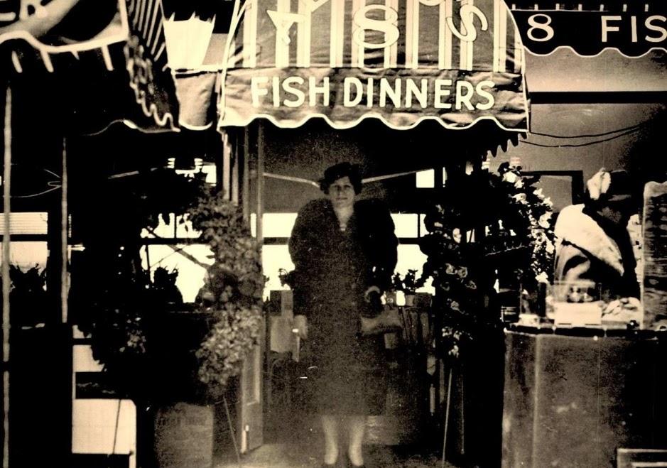 Woman dressed in formal clothing stands&nbsp;in&nbsp;front&nbsp;of&nbsp;a&nbsp;restaurant&nbsp;awning&nbsp;that&nbsp;reads&nbsp;“fish&nbsp;dinners,”&nbsp;circa 1950.&nbsp;