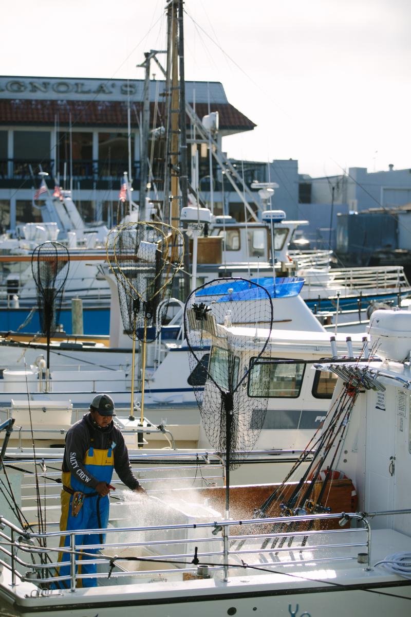 A fisherman&nbsp;sprays&nbsp;water&nbsp;on&nbsp;his&nbsp;boat,&nbsp;docked&nbsp;at&nbsp;a&nbsp;berth.