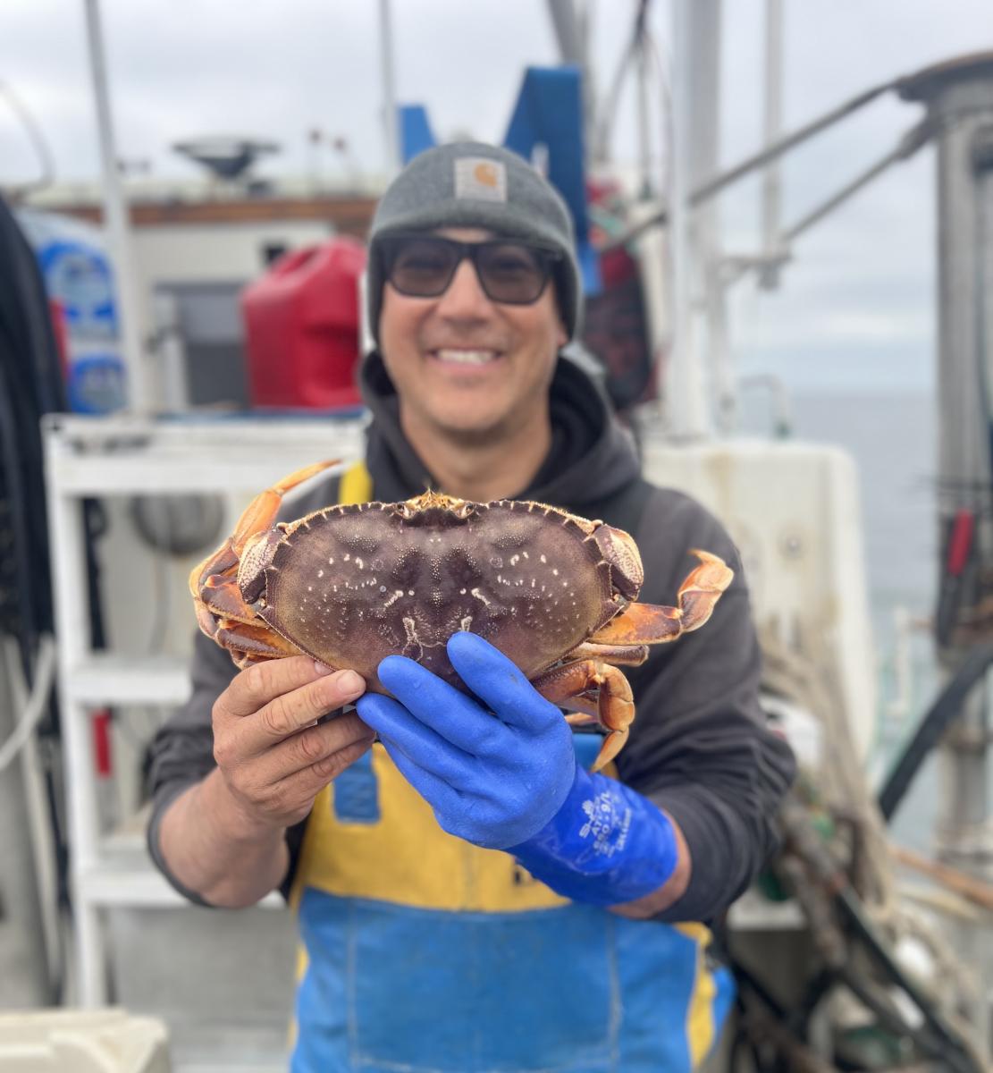 A&nbsp;fisherman&nbsp;holds&nbsp;up&nbsp;a&nbsp;crab,&nbsp;smiling.&nbsp;