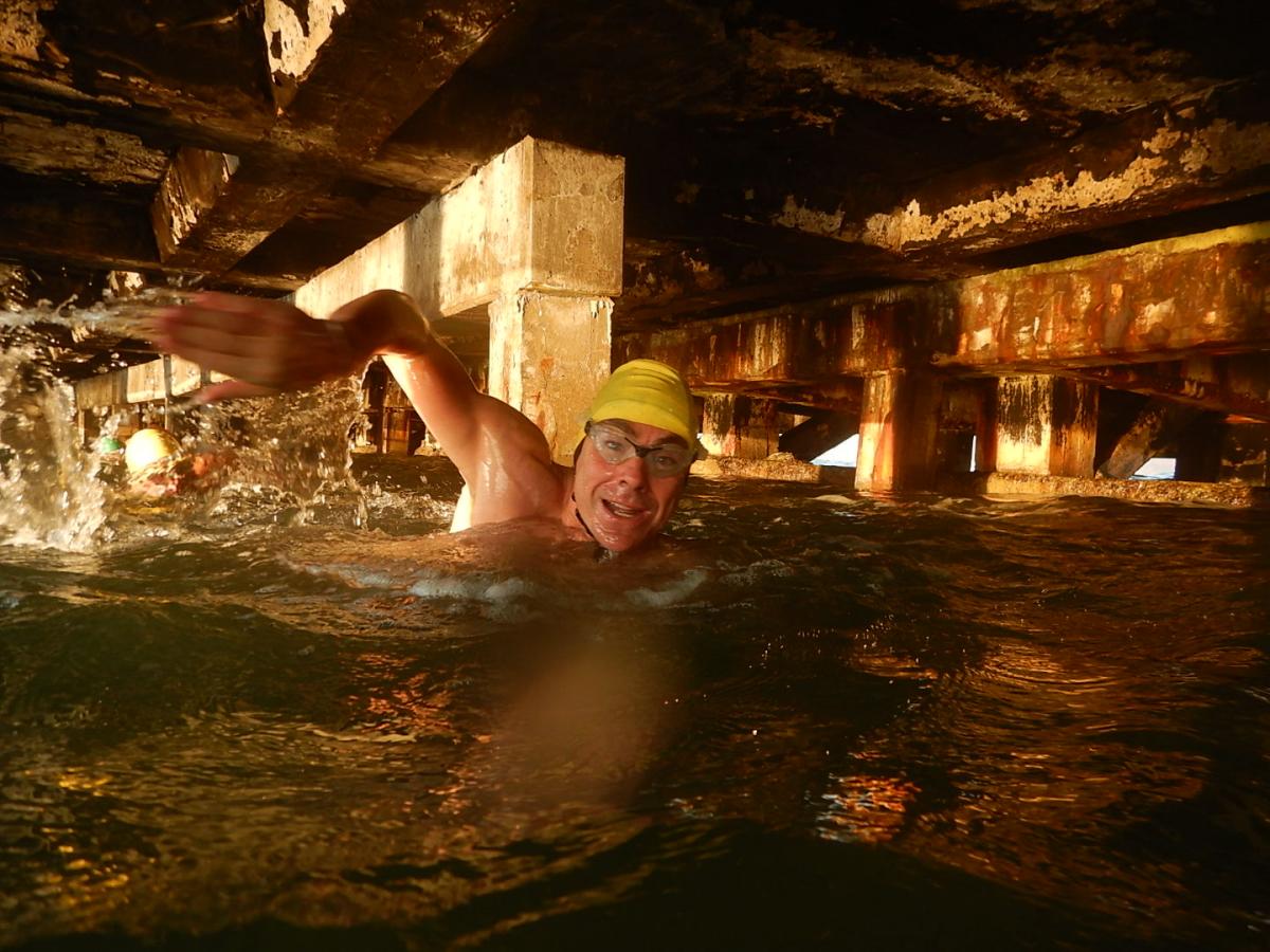 A man swimming below a pier.