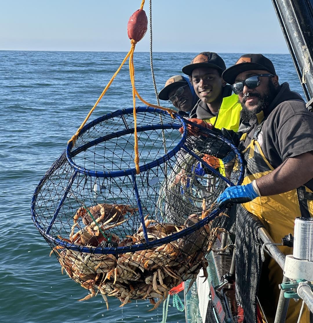 A&nbsp;group&nbsp;of&nbsp;fishermen&nbsp;smiles&nbsp;next&nbsp;to&nbsp;a&nbsp;loaded&nbsp;crab&nbsp;pot.&nbsp;