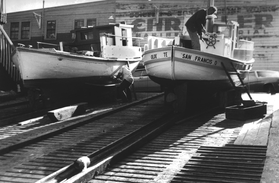 Historic image of men working on boats that are pulled up on wooden ramps.&nbsp;