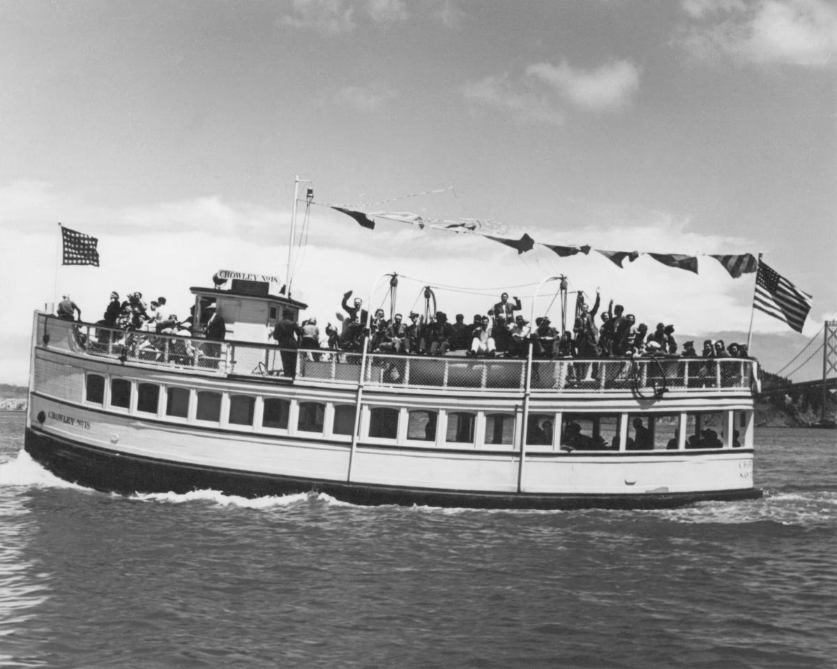 Historic image of a tour boat with a smiling crowd on the top deck. 
