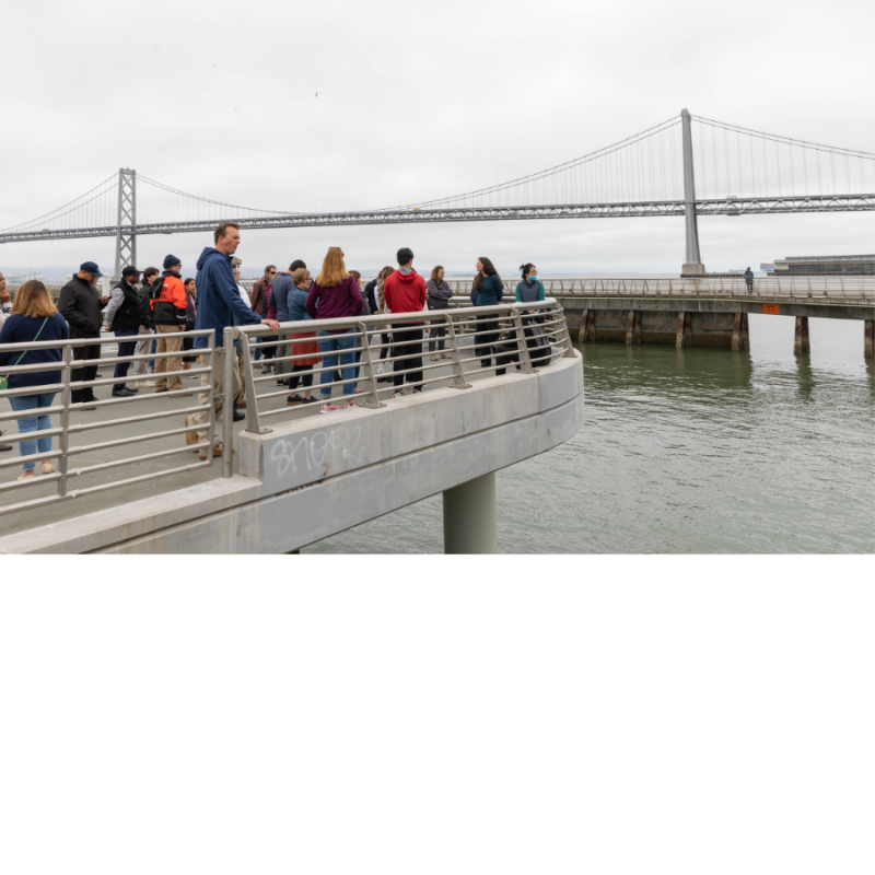 People standing on a pier overlooking the water and Bay Bridge