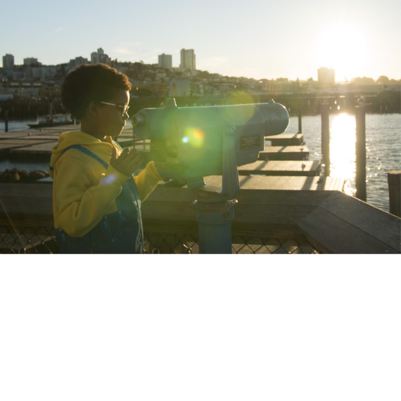 Child looks through binoculars outside on the waterfront