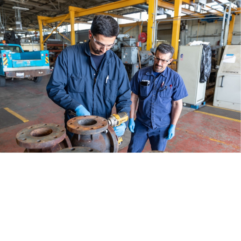 Man observes his trainee drill into a metal pipe.
